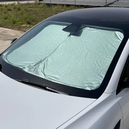 Tesla windshield sunshade unfolded and positioned across the front windshield, showing heat-reflective silver exterior